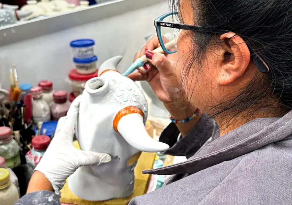 Artist painting intricate designs on pottery piece.